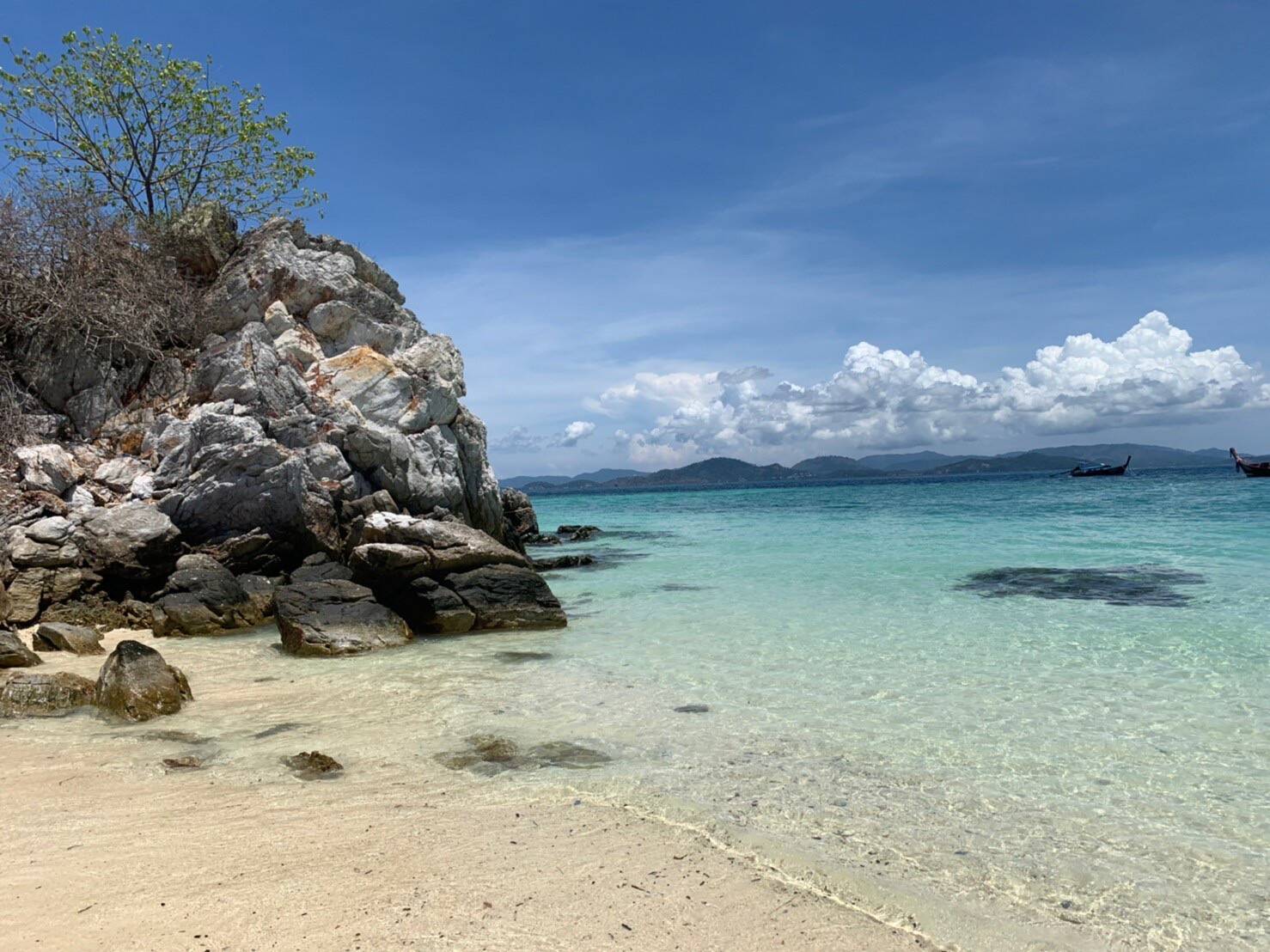 Clear turquoise water and rocky point at Khai Island with longtail boats in the distance