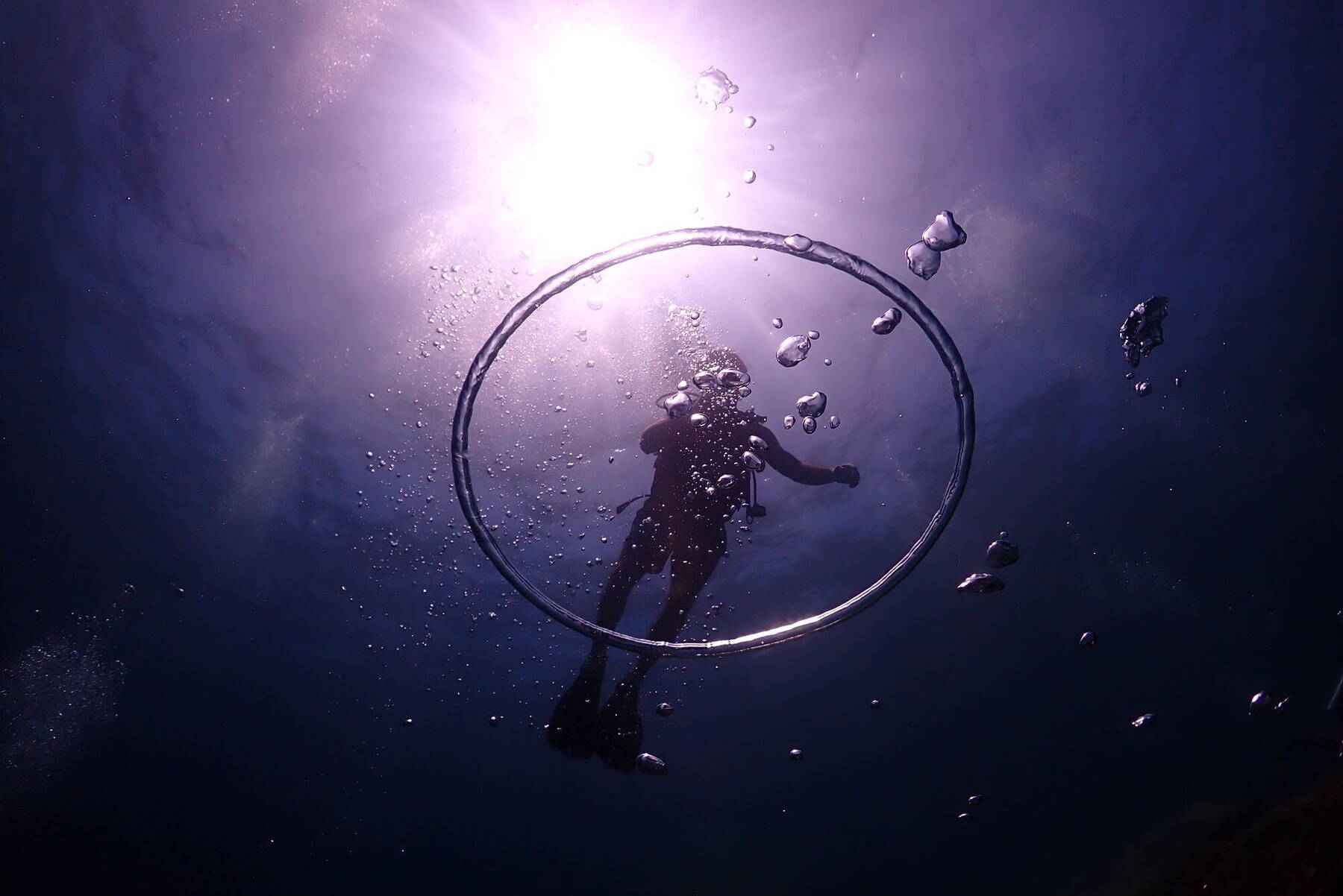 Silhouette of a diver beneath a ring of bubbles